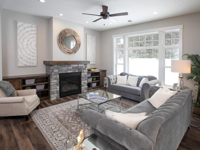 living room with a stone fireplace, dark hardwood / wood-style floors, and ceiling fan