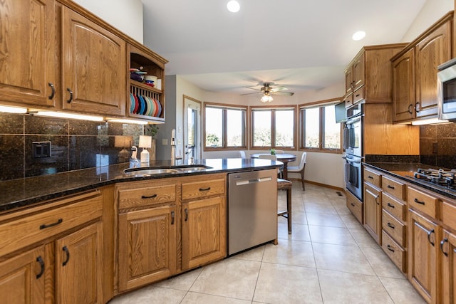 kitchen featuring decorative backsplash, appliances with stainless steel finishes, ceiling fan, light tile patterned floors, and dark stone countertops