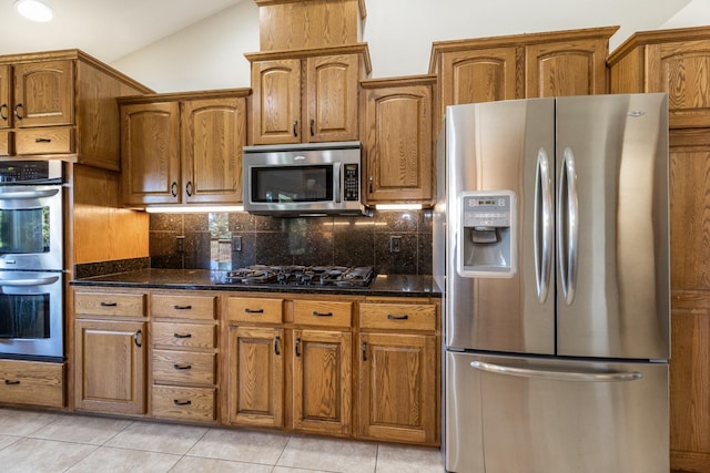 kitchen featuring light tile patterned flooring, appliances with stainless steel finishes, lofted ceiling, and dark stone countertops