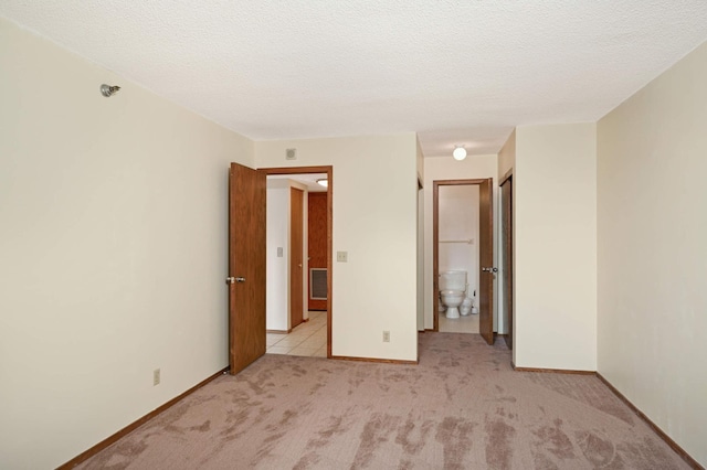 unfurnished bedroom with a textured ceiling, connected bathroom, and light colored carpet