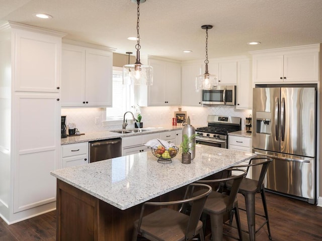 kitchen featuring appliances with stainless steel finishes, dark wood-type flooring, white cabinets, a center island, and sink