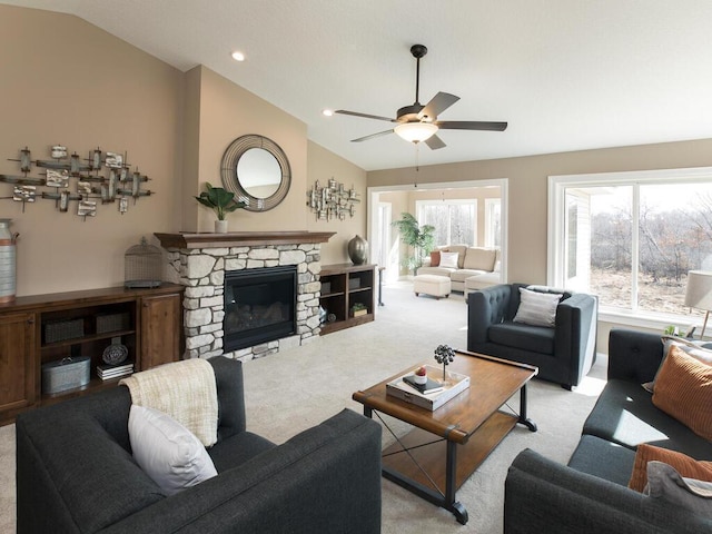 carpeted living room featuring a stone fireplace, lofted ceiling, and ceiling fan