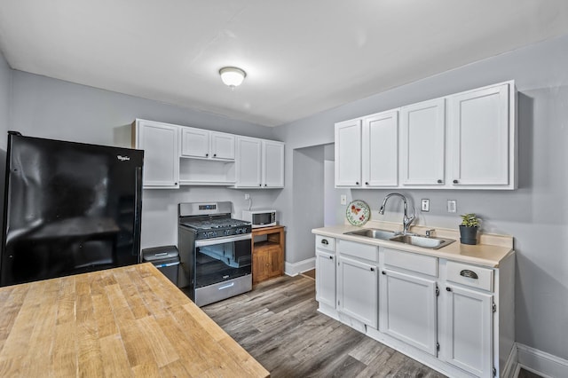 kitchen with black fridge, gas stove, sink, hardwood / wood-style flooring, and white cabinets