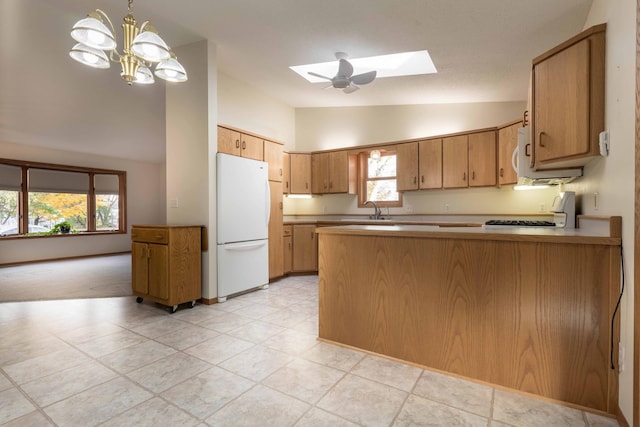 kitchen with white appliances, a healthy amount of sunlight, vaulted ceiling with skylight, and kitchen peninsula