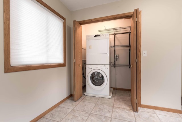 laundry area featuring stacked washer and dryer, light tile patterned floors, and a wealth of natural light