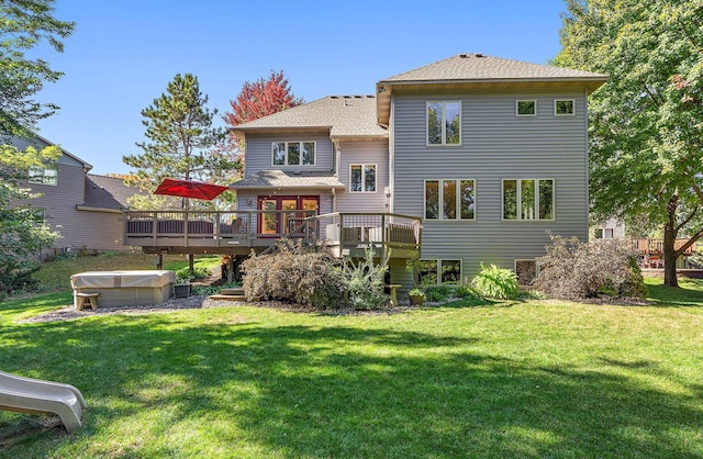 rear view of house with a lawn, a hot tub, and a deck