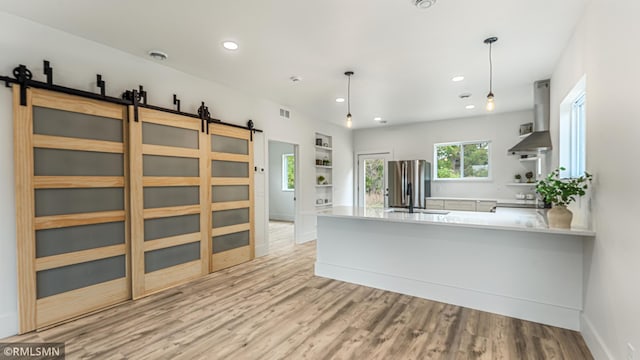 kitchen with stainless steel fridge, hanging light fixtures, range hood, and a barn door