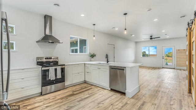 kitchen with light wood-type flooring, white cabinetry, wall chimney exhaust hood, appliances with stainless steel finishes, and decorative light fixtures