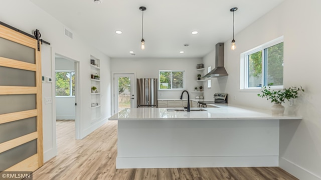 kitchen featuring pendant lighting, kitchen peninsula, wall chimney range hood, and a barn door