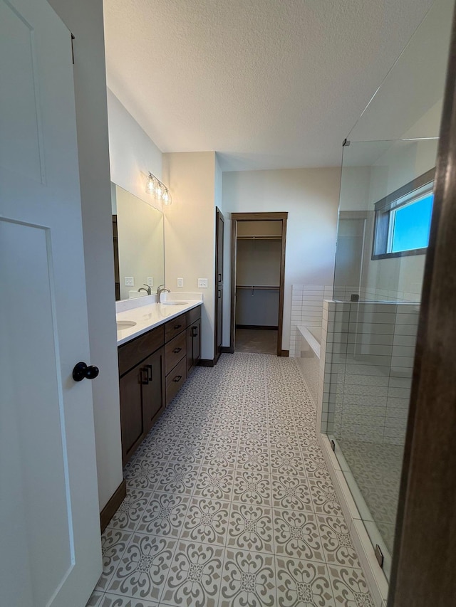 13077 Opal St NE, Blaine, MN 55449 - bathroom featuring baseboards, tiled shower, double vanity, a sink, and a textured ceiling