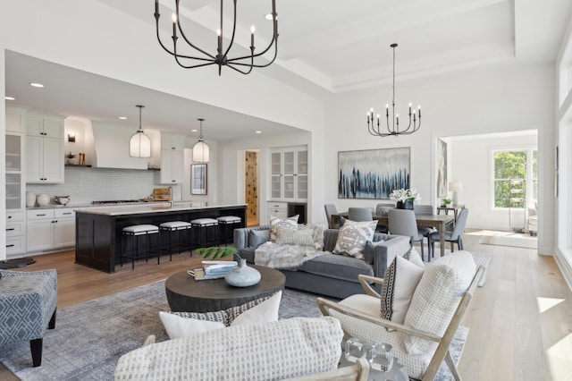 living room featuring a notable chandelier, light wood-type flooring, a raised ceiling, and a high ceiling