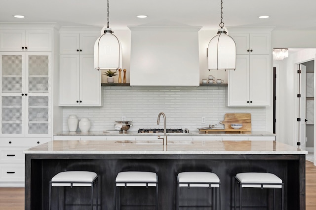 kitchen featuring a kitchen island with sink, light stone countertops, and white cabinets