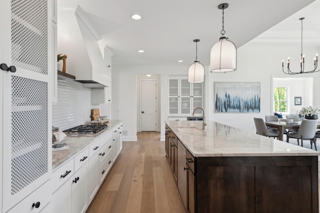 kitchen with light wood-type flooring, white cabinets, decorative backsplash, decorative light fixtures, and dark brown cabinetry