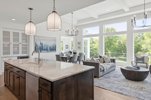 kitchen featuring light hardwood / wood-style floors, light stone counters, decorative light fixtures, a center island with sink, and sink