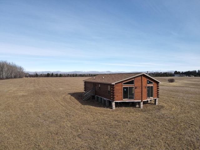exterior space featuring a rural view, roof with shingles, and log exterior