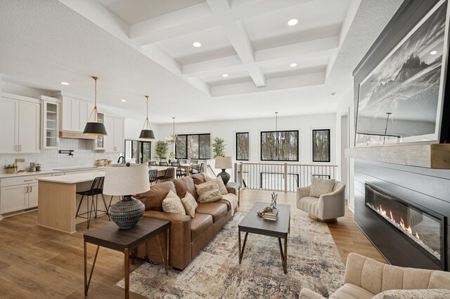 living area featuring beamed ceiling, wood finished floors, coffered ceiling, and a glass covered fireplace