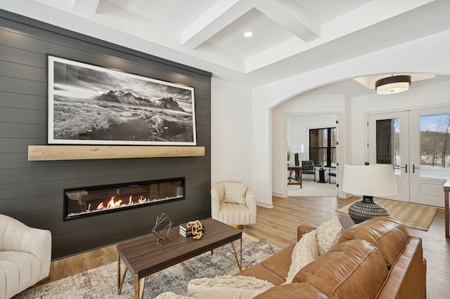 living room featuring wood finished floors, coffered ceiling, beam ceiling, arched walkways, and a large fireplace