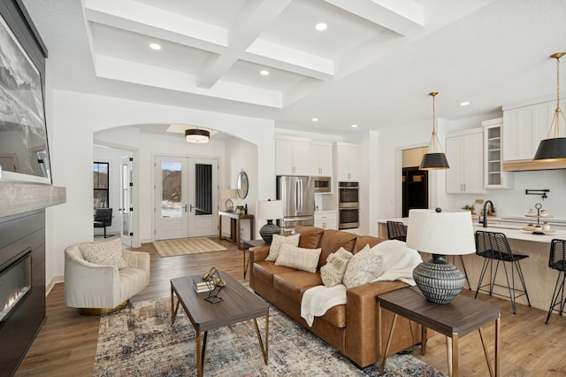 living area with beamed ceiling, arched walkways, and light wood finished floors