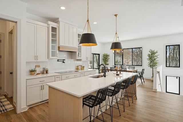 kitchen with a kitchen bar, light wood-style flooring, a sink, backsplash, and black electric stovetop