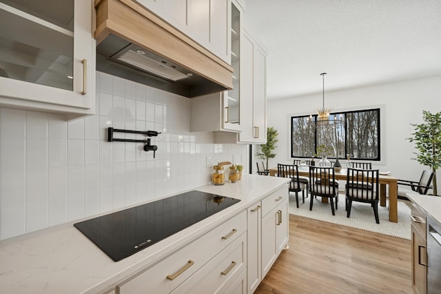 kitchen featuring backsplash, premium range hood, light wood-type flooring, white cabinets, and black electric cooktop