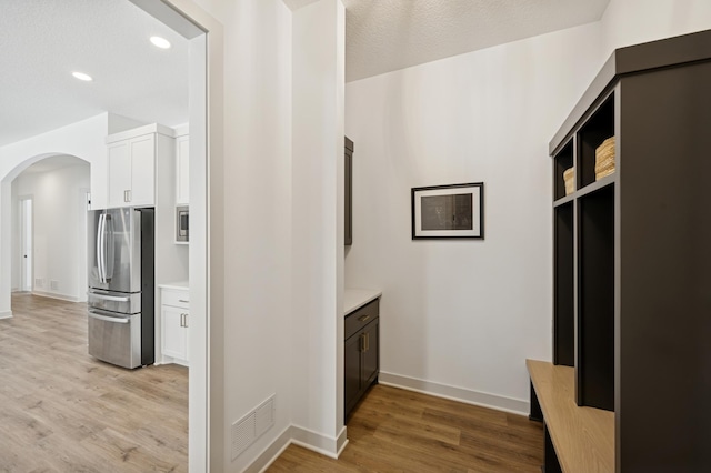 interior space with visible vents, light wood-style flooring, freestanding refrigerator, arched walkways, and white cabinets