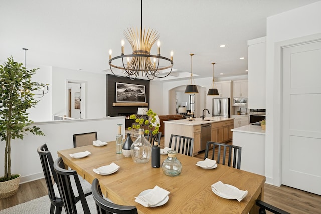 dining space with a notable chandelier, a warm lit fireplace, wood finished floors, recessed lighting, and arched walkways