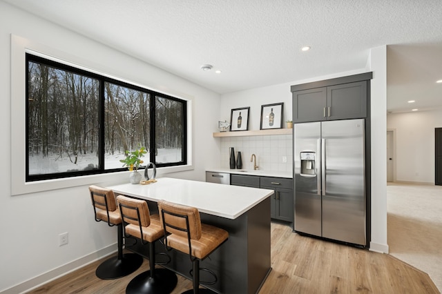 kitchen with a breakfast bar, a sink, backsplash, appliances with stainless steel finishes, and light countertops