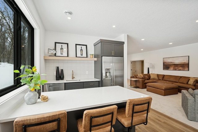 kitchen with open shelves, a sink, stainless steel appliances, light countertops, and a kitchen breakfast bar