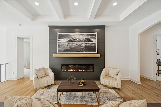 living area with beamed ceiling, a large fireplace, baseboards, and wood finished floors