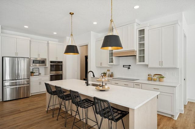 kitchen featuring light wood-style flooring, an island with sink, a sink, a kitchen breakfast bar, and appliances with stainless steel finishes