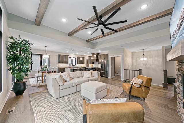 living room with ceiling fan with notable chandelier, light hardwood / wood-style floors, and lofted ceiling with beams