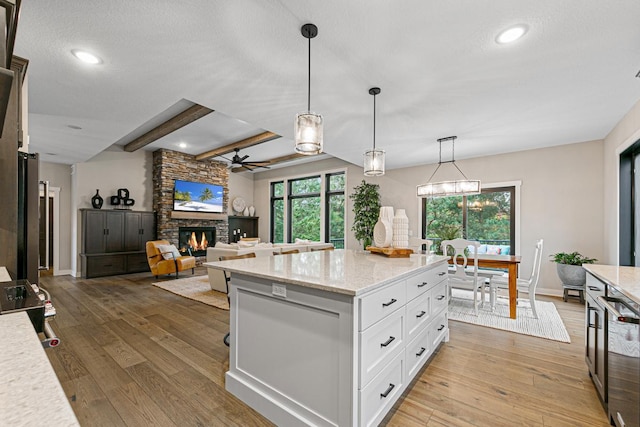 kitchen featuring light stone counters, white cabinets, pendant lighting, a stone fireplace, and light wood-type flooring