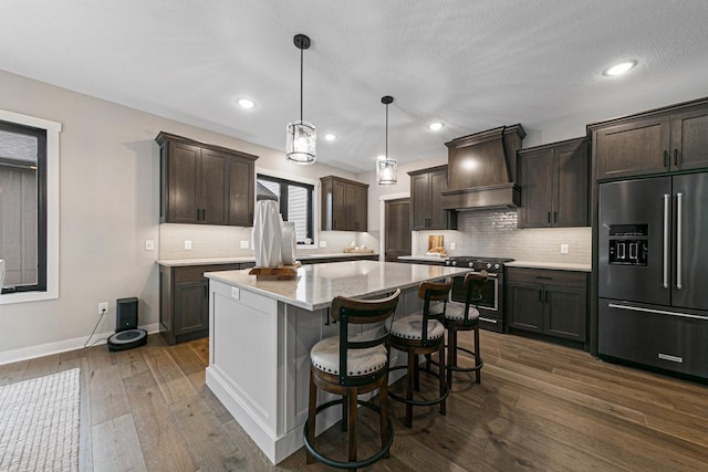 kitchen featuring a center island, dark hardwood / wood-style floors, stainless steel appliances, decorative light fixtures, and premium range hood