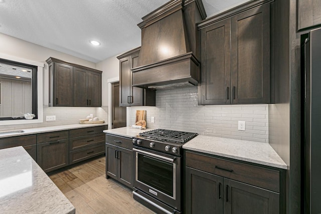 kitchen featuring light stone countertops, gas range, light hardwood / wood-style flooring, and custom range hood