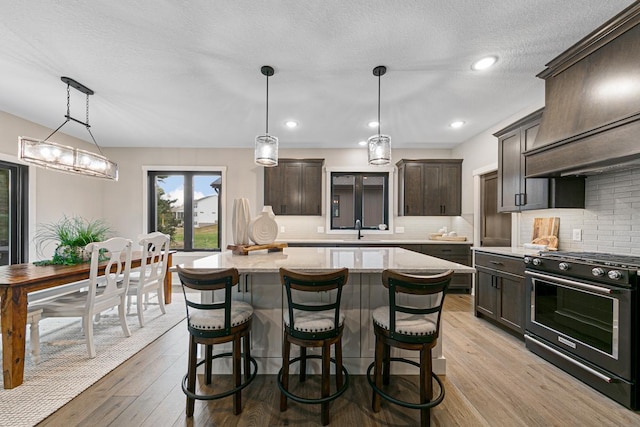 kitchen featuring pendant lighting, light wood-type flooring, dark brown cabinets, a center island, and stainless steel range