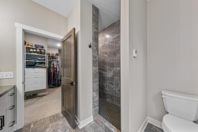 bathroom featuring a textured ceiling, tiled shower, vanity, and toilet