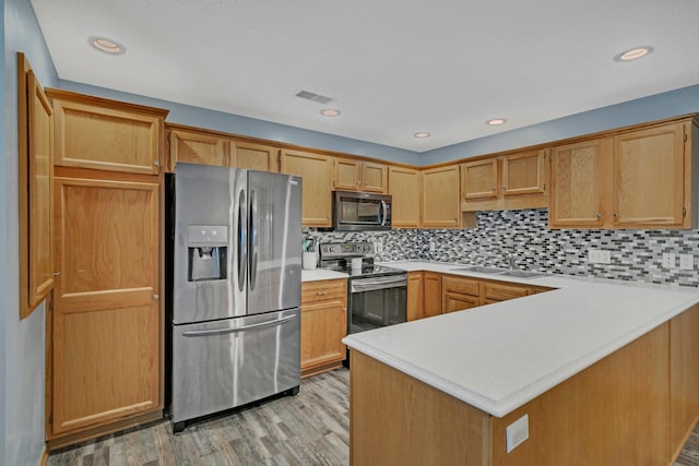 kitchen with kitchen peninsula, tasteful backsplash, sink, light hardwood / wood-style floors, and stainless steel appliances