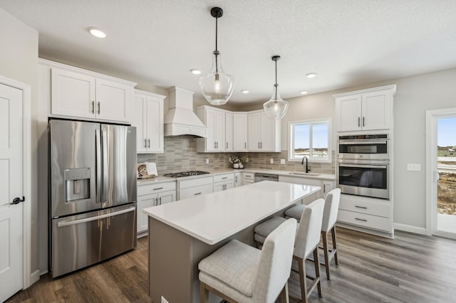 kitchen featuring a kitchen island, custom range hood, white cabinetry, and stainless steel appliances