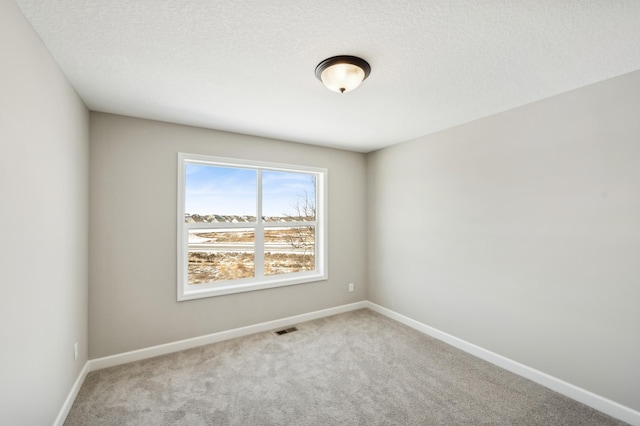 spare room with a textured ceiling, carpet flooring, visible vents, and baseboards