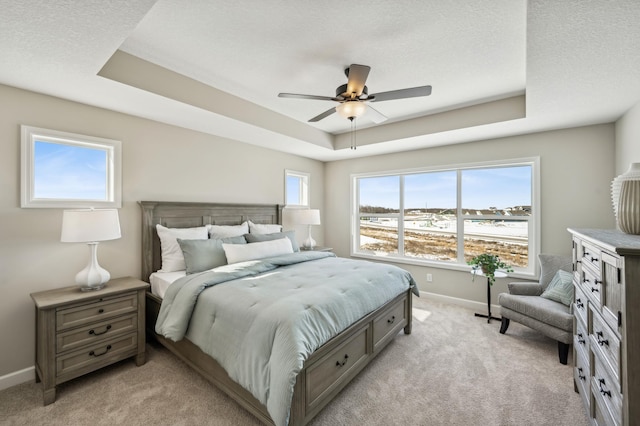 bedroom with a textured ceiling, light carpet, a ceiling fan, baseboards, and a raised ceiling