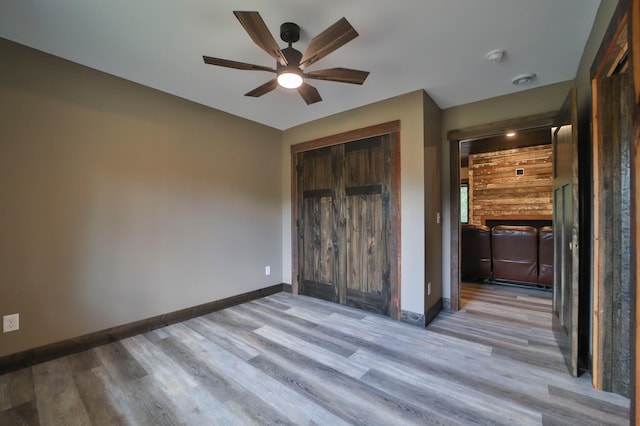 unfurnished bedroom with a closet, wood walls, light hardwood / wood-style floors, and ceiling fan