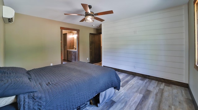 bedroom featuring a wall mounted AC, hardwood / wood-style floors, ceiling fan, and ensuite bath