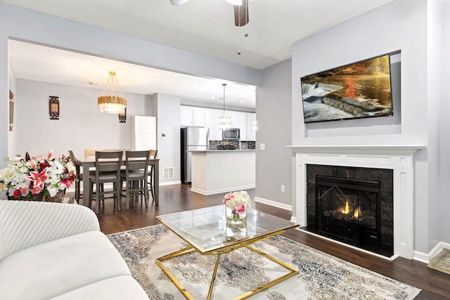 living room with a textured ceiling, ceiling fan, a fireplace, and dark hardwood / wood-style floors