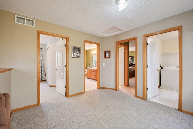 hallway with light carpet, washer / clothes dryer, and a textured ceiling