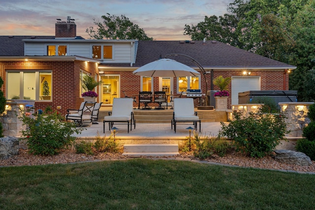 rear view of property with brick siding, a chimney, a hot tub, a patio area, and a garage