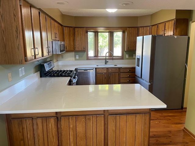 kitchen with sink, stainless steel appliances, kitchen peninsula, and dark hardwood / wood-style flooring