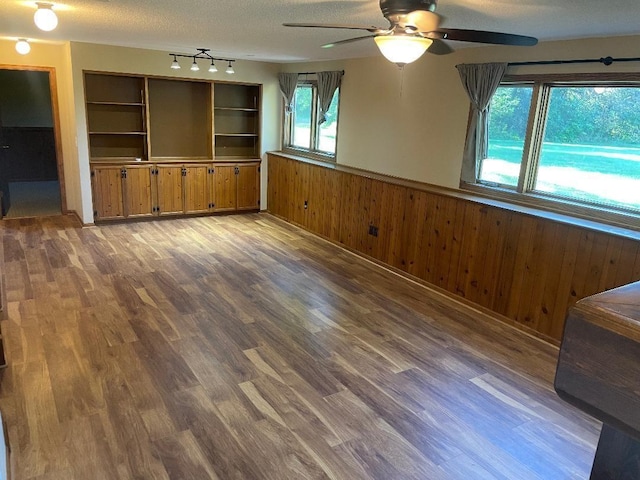 unfurnished living room featuring a textured ceiling, wood walls, and dark wood-type flooring