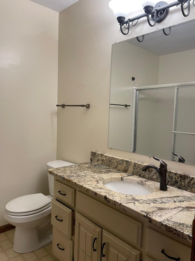 bathroom featuring a textured ceiling, vanity, toilet, and a shower with shower door