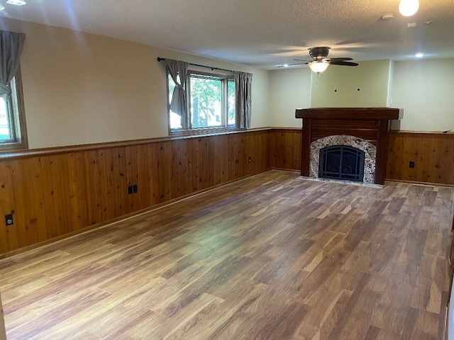 unfurnished living room featuring ceiling fan, hardwood / wood-style flooring, wood walls, and a textured ceiling