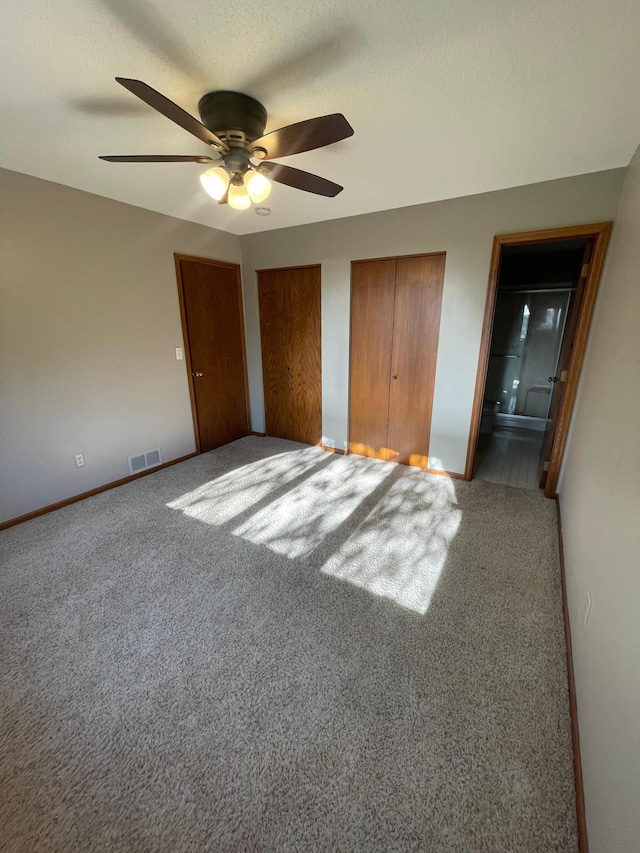 unfurnished bedroom with carpet floors, connected bathroom, two closets, and ceiling fan